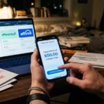 A person confirms a purchase on a smartphone showing “4 payments of $50 interest-free,” while a laptop in the background displays Klarna, Afterpay, and Affirm options. Past-due bills and late fee notices are spread across the desk.